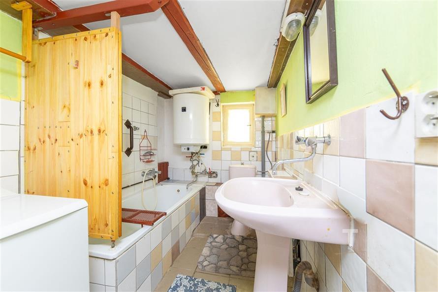 Koupelna s keramickými obklady, dřevěnou sprchovou zástěnou a vestavěnou vanou, s výrazným světlým nástěnným nátěrem a elektrickým bojlerem.