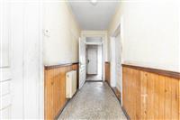 Úzká chodba s dřevěným obložením, světlé stěny, linoleum na podlaze, několik dveří vedoucích do dalších místností, starší stavba.