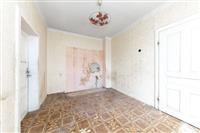 Neudržovaný pokoj s dlažbou a bílými zdmi, chybějící omítka a nástěnný lustr, vhodný k rekonstrukci.