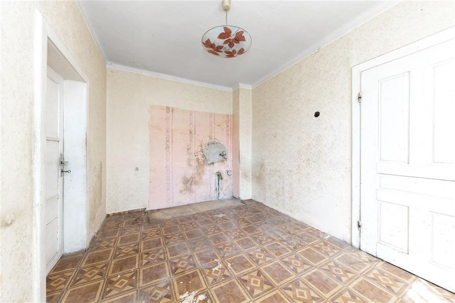 Neudržovaný pokoj s dlažbou a bílými zdmi, chybějící omítka a nástěnný lustr, vhodný k rekonstrukci.