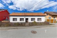 Rodinný dům s tradiční fasádou, šikmou střechou a dřevěným plotem, nachází se v klidné ulici, ideální pro rekonstrukci.