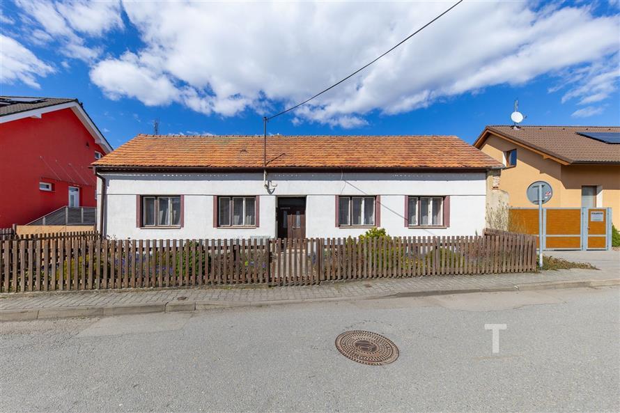 Rodinný dům s tradiční fasádou, šikmou střechou a dřevěným plotem, nachází se v klidné ulici, ideální pro rekonstrukci.