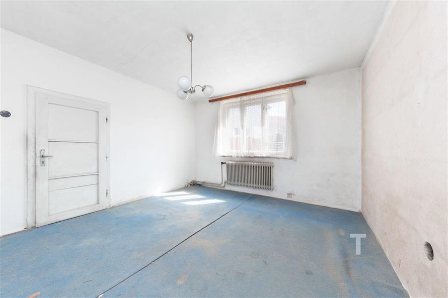 Světlý pokoj s velkým oknem, starší koberce a bílá omítka, možnost rekonstrukce, klidné prostředí.