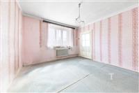 Prostorná ložnice s růžovými tapetami, velkým oknem a starším radiátorem, připravena k rekonstrukci a úpravám podle vlastních představ.