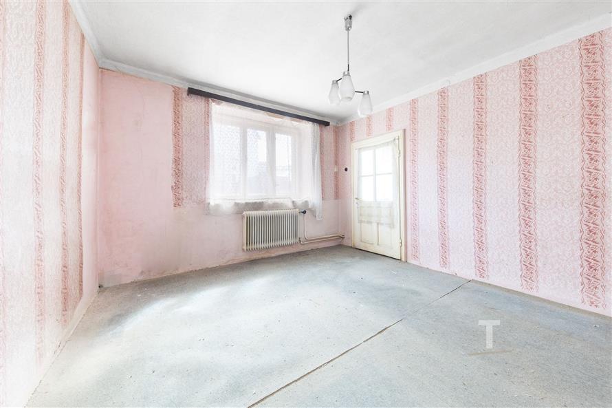 Prostorná ložnice s růžovými tapetami, velkým oknem a starším radiátorem, připravena k rekonstrukci a úpravám podle vlastních představ.