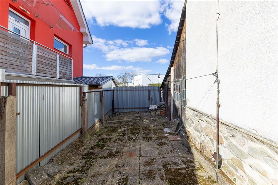 Zahradní prostor s kamennou dlažbou, ohraničený plotem, vyžadující renovaci. Vhodný pro modernizaci a úpravu dle vlastního stylu.