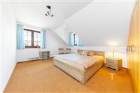 Prostorná ložnice s dřevěnou postelí, velká okna s modrými závěsy, světlý interiér, vestavěné skříně, koberec na podlaze