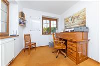 Domácí kancelář s dřevěným nábytkem, kobercovou podlahou a velkým oknem. Světlé prostory ideální pro práci nebo studium.
