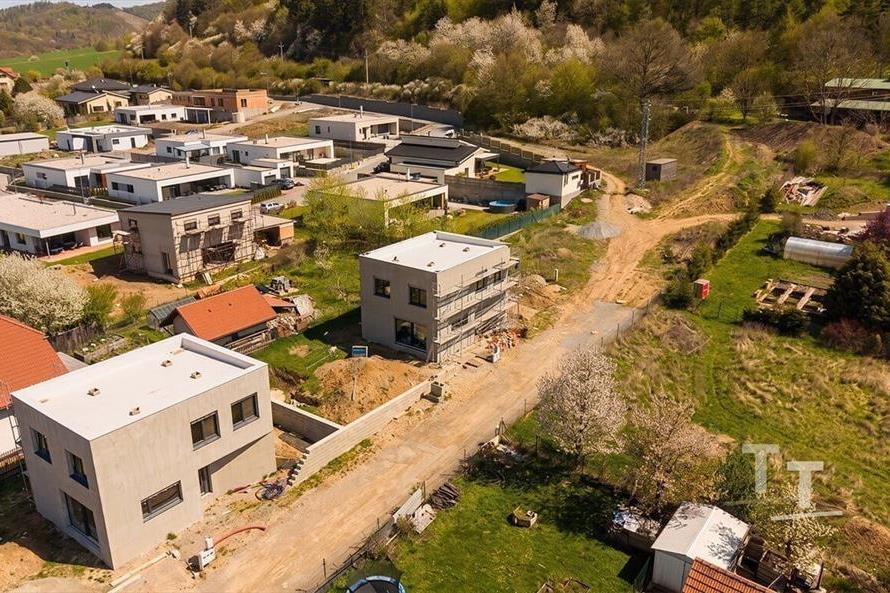 Pohled na moderní rezidenční čtvrť s novostavbami uprostřed zeleně, kde převažují ploché střechy a minimalistický styl v klidné lokalitě.