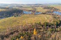 Pohled na rozsáhlý stavební pozemek na prodej s malebným výhledem na přírodní krajinu a blízký les, ideální pro klidné bydlení.