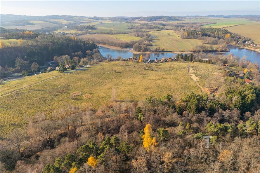 Pohled na rozsáhlý stavební pozemek na prodej s malebným výhledem na přírodní krajinu a blízký les, ideální pro klidné bydlení.