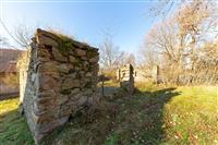 Ruiny kamenné stavby obklopené trávníkem a stromy, ideální pro rekonstrukci, nabízejí potenciál pro moderní bydlení na klidném místě