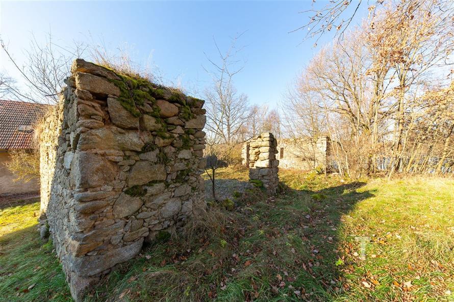 Ruiny kamenné stavby obklopené trávníkem a stromy, ideální pro rekonstrukci, nabízejí potenciál pro moderní bydlení na klidném místě