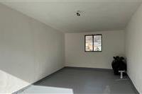 Prázdná garáž s betonovou podlahou, malým oknem a světlými zdmi, ideální pro skladování nebo parkování.