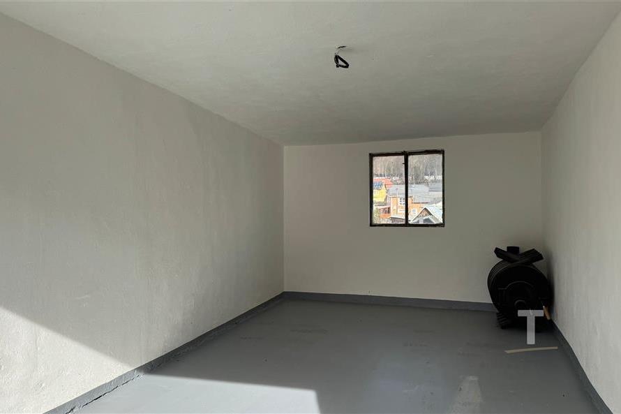 Prázdná garáž s betonovou podlahou, malým oknem a světlými zdmi, ideální pro skladování nebo parkování.