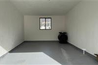 Prázdná garáž s betonovou podlahou, světlý prostor s malým oknem, v dobrém stavu.