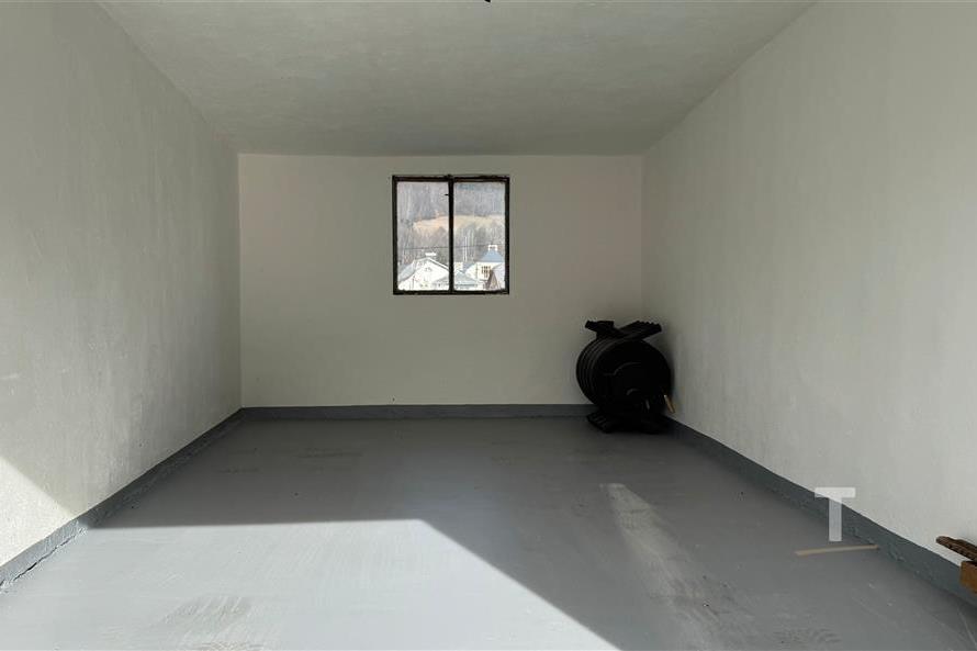 Prázdná garáž s betonovou podlahou, světlý prostor s malým oknem, v dobrém stavu.