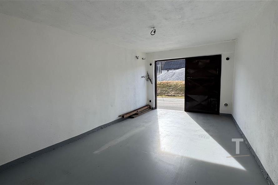 Prostorná garáž s betonovou podlahou, bílými stěnami a masivními kovovými vraty, ideální pro bezpečné parkování vozidla.