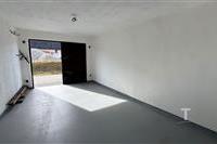 Prázdná garáž s betonovou podlahou, nově vymalovaná, dobře osvětlená s otevřenými dveřmi, poskytuje prostor pro parkování nebo skladování