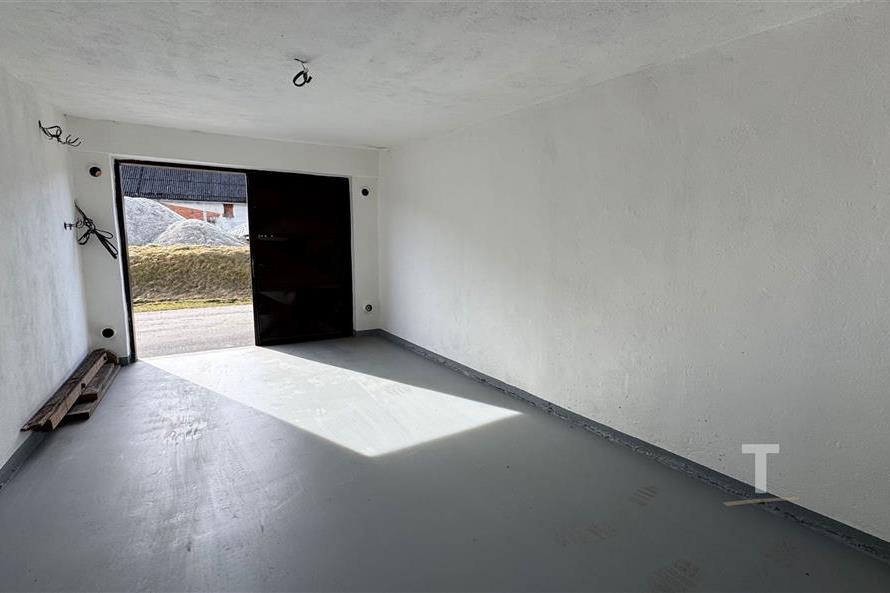 Prázdná garáž s betonovou podlahou, nově vymalovaná, dobře osvětlená s otevřenými dveřmi, poskytuje prostor pro parkování nebo skladování