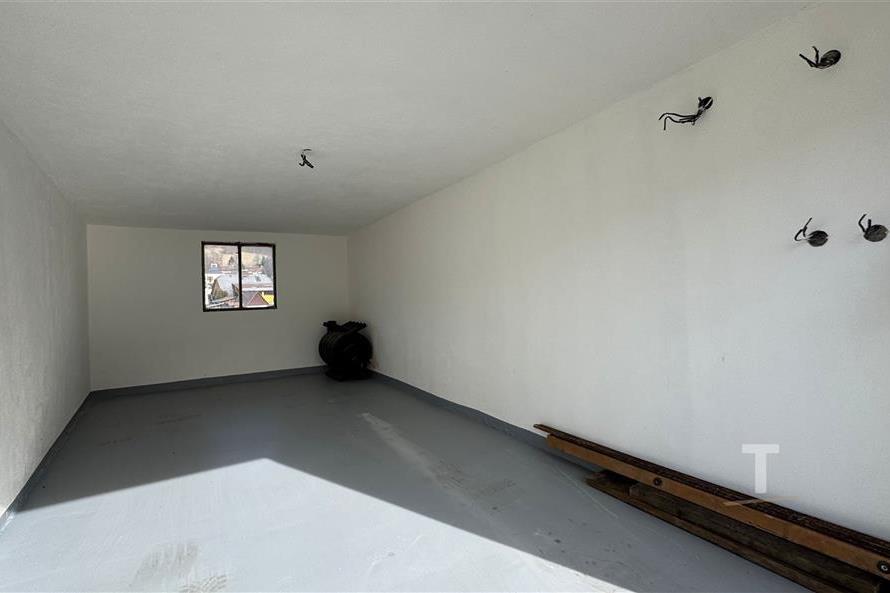 Prázdná garáž s betonovou podlahou, bílými stěnami a malým čtvercovým oknem, připravená k přizpůsobení.