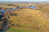 Letecký pohled na rozsáhlý pozemek s výhledem na jezero, obklopený zelení a přírodou, ideální pro výstavbu rodinných domů nebo rekreačních objektů.