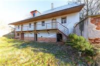 Částečně rekonstruovaný venkovský dům s cihelnou fasádou a dřevěnou terasou, umístěný na klidném pozemku s přírodním okolím.