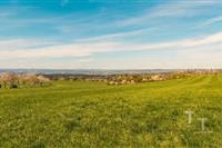 Zelená rozlehlá louka s výhledem na vzdálené kopce a modrou oblohu, ideální pro stavbu, klidná a malebná lokalita v přírodním prostředí.