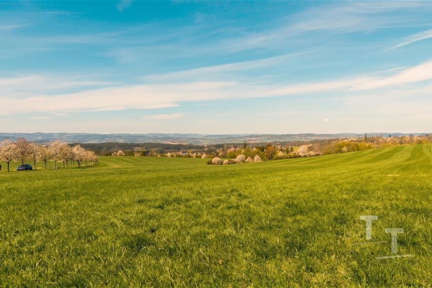 Zelená rozlehlá louka s výhledem na vzdálené kopce a modrou oblohu, ideální pro stavbu, klidná a malebná lokalita v přírodním prostředí.