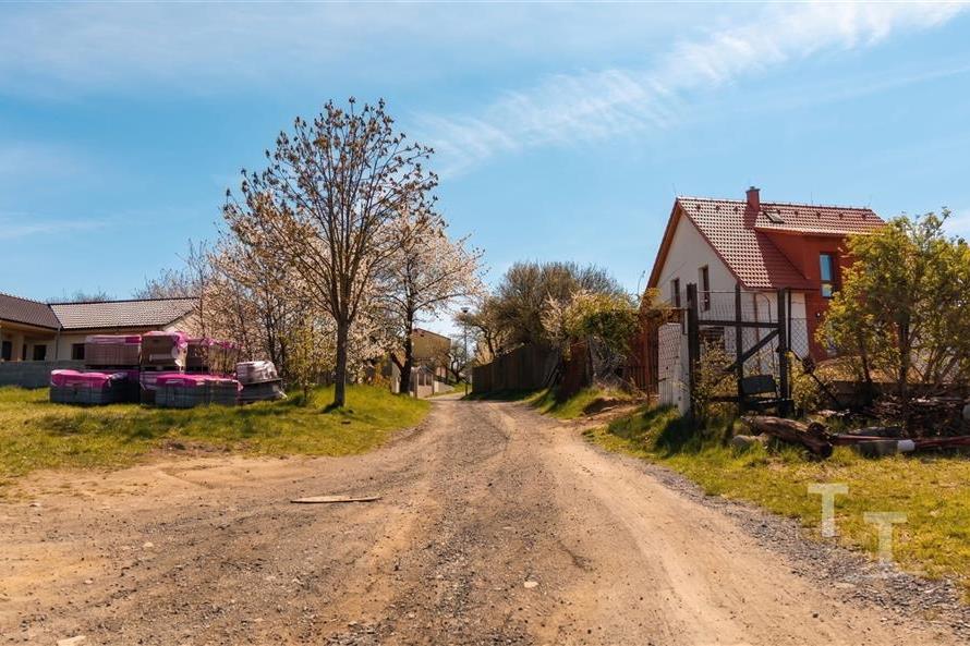 Příjezdová cesta k rodinnému domu s červenou střechou, okolní stromy v rozkvětu, klidná lokalita, prostor pro úpravy, potenciál venkovského bydlení.