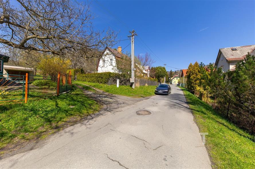 Příjezdová cesta u rodinného domu s udržovanou zahradou, klidná lokalita s přírodními prvky, vhodné pro rodinné bydlení.