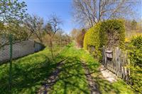 Zahrada s travnatým pozemkem, dřevěným plotem a stromy, ideální pro klidný pobyt na venkově, slunné místo vhodné pro rekreační vyžití.