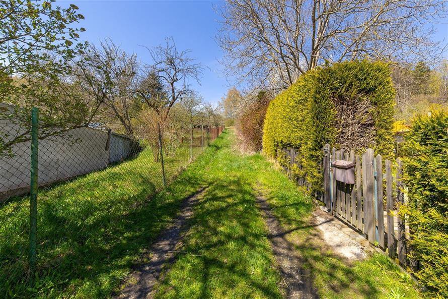 Zahrada s travnatým pozemkem, dřevěným plotem a stromy, ideální pro klidný pobyt na venkově, slunné místo vhodné pro rekreační vyžití.