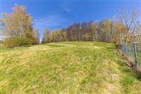 Prázdný stavební pozemek s výhledem na lesy, oplocený, vhodný pro rodinný dům, mírně svažitý terén, klidná lokalita blízko přírody