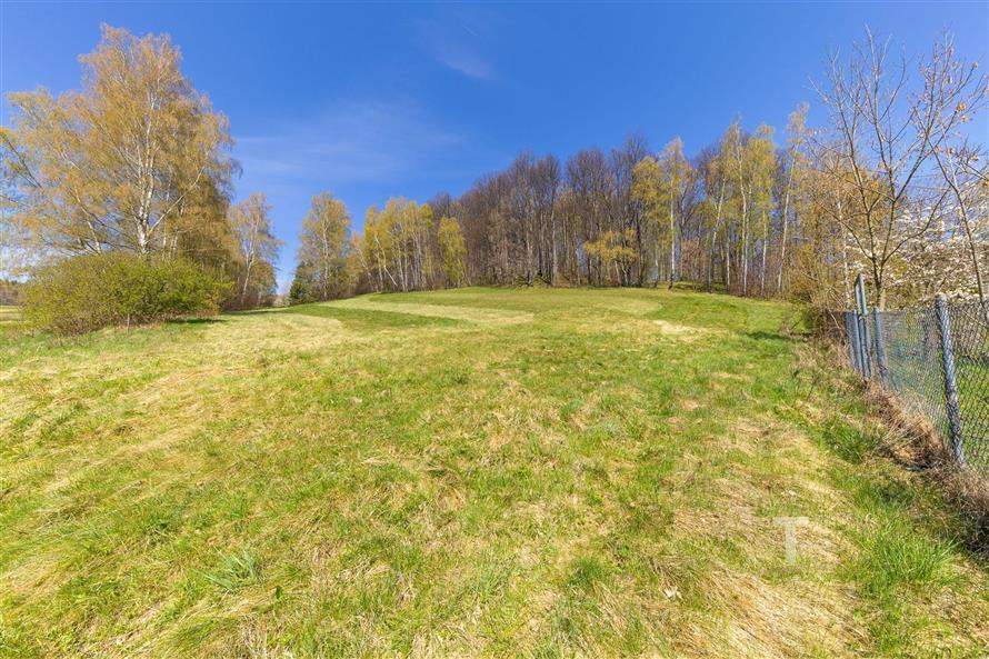 Prázdný stavební pozemek s výhledem na lesy, oplocený, vhodný pro rodinný dům, mírně svažitý terén, klidná lokalita blízko přírody